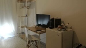 A small, sparsely furnished room with a desk, a computer, and a refrigerator. - Gatto Bianco Picone 19 (Bari)