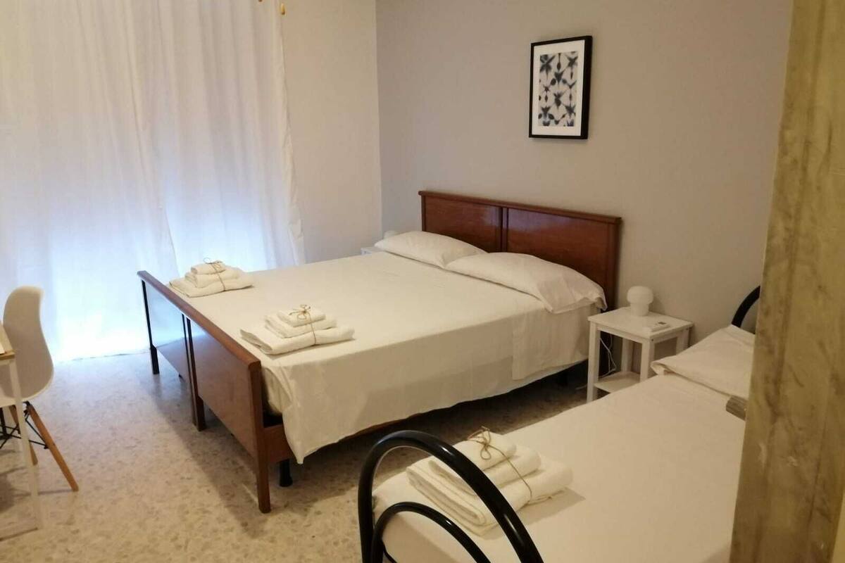 A hotel room with two beds, a small bedside table, a chair, and a window with curtains.