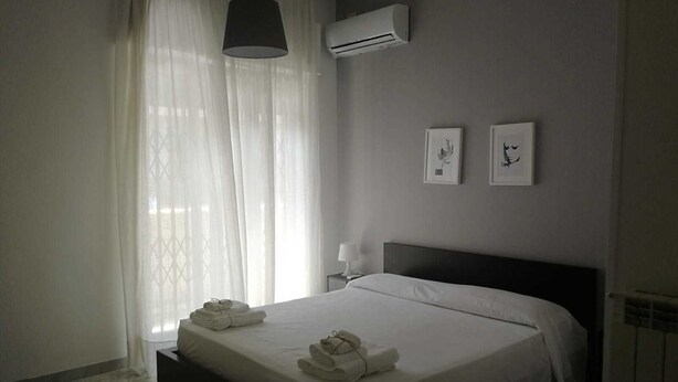 A bedroom with a bed, white curtains, an air conditioning unit, and two framed pictures on the wall. - Gatto Bianco Picone 19 (Bari)