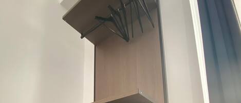 A modern, built-in storage unit with a wooden finish, featuring a shelf, a cylindrical object, and a drawer.