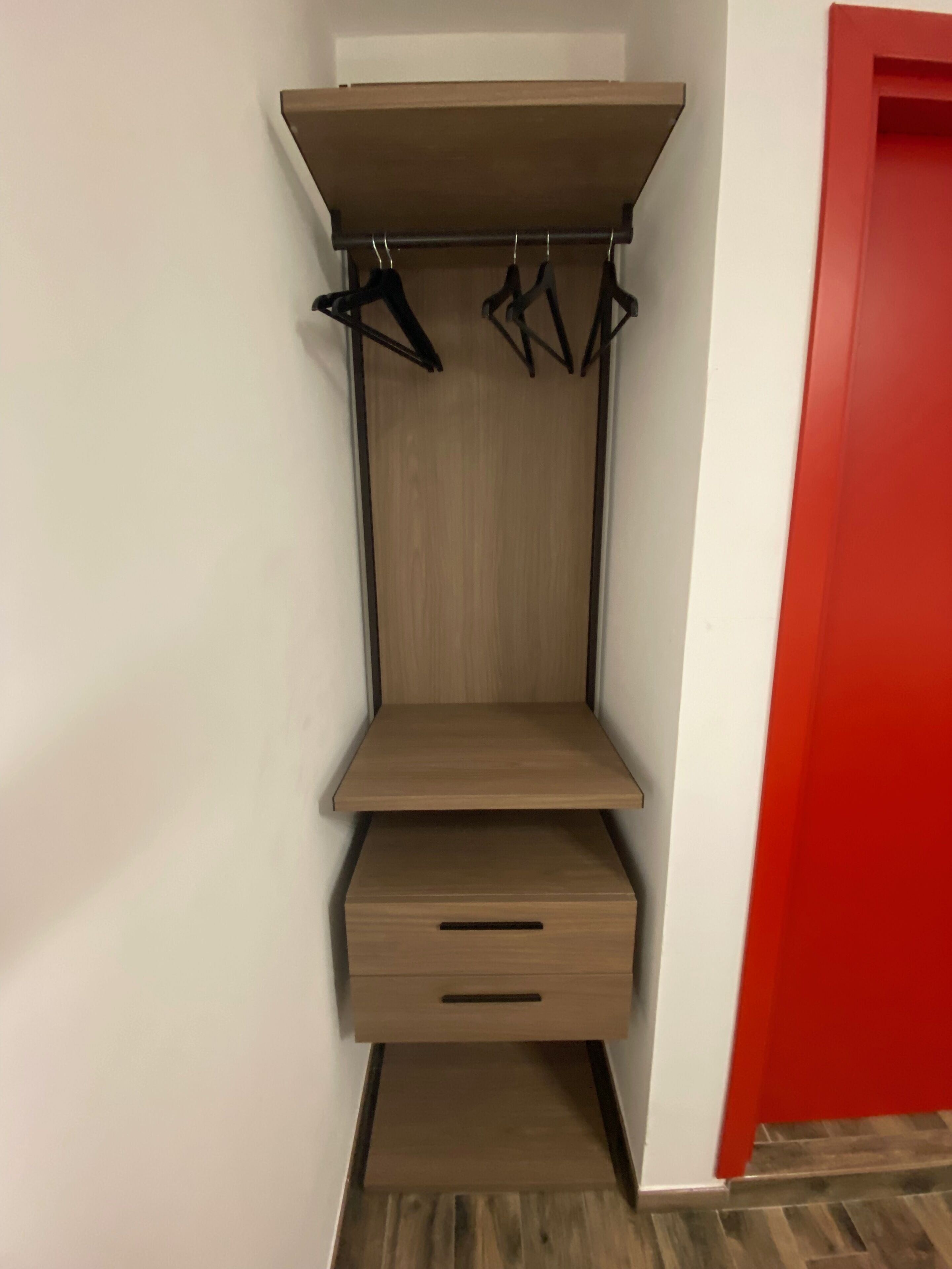 A corner closet with a hanging rod, a shelf, and a drawer unit.