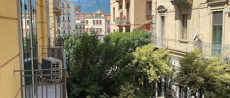 A narrow street flanked by multi-story buildings with balconies, trees, and a clear sky.