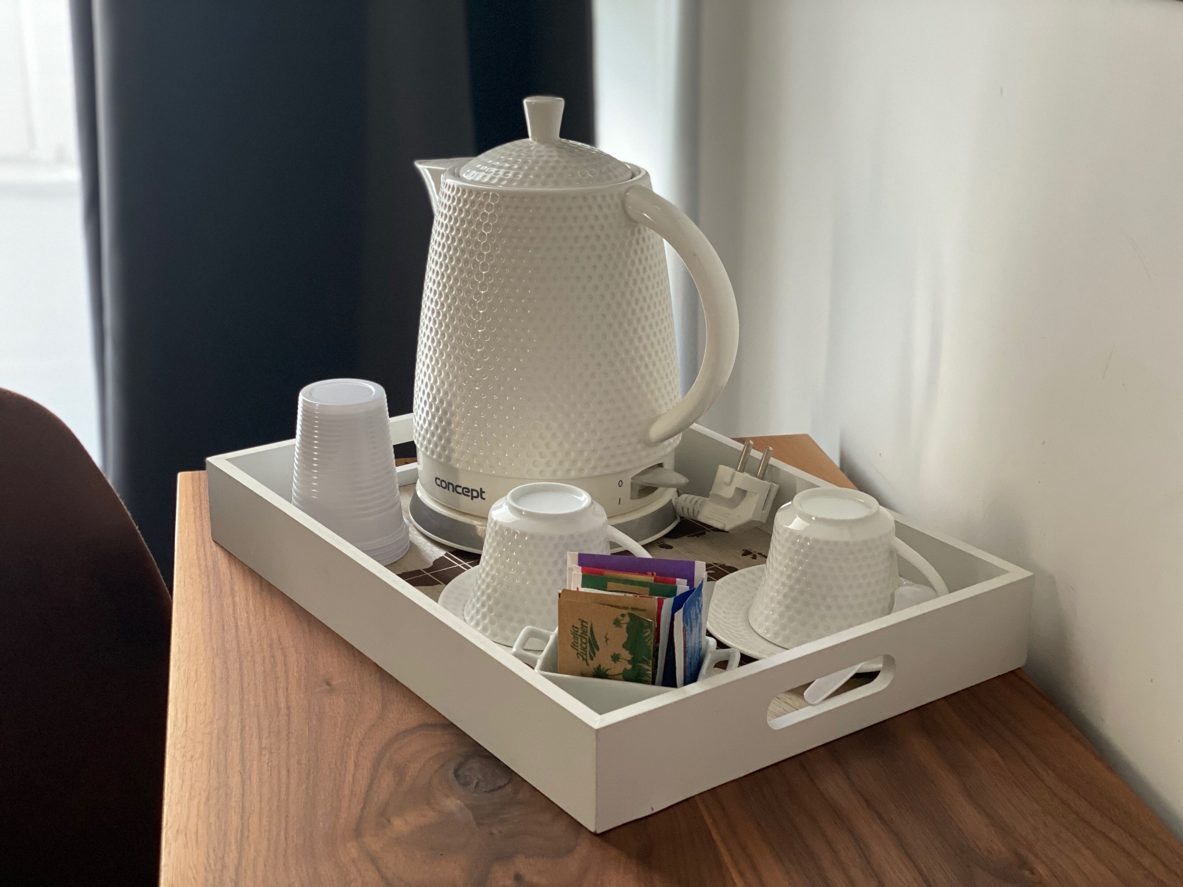 A tray with a white coffee maker, several white cups, and a box of books on a wooden table.