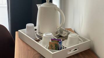 Een dienblad met een witte koffiezetapparaat, meerdere witte kopjes en een stapel boeken op een houten tafel.