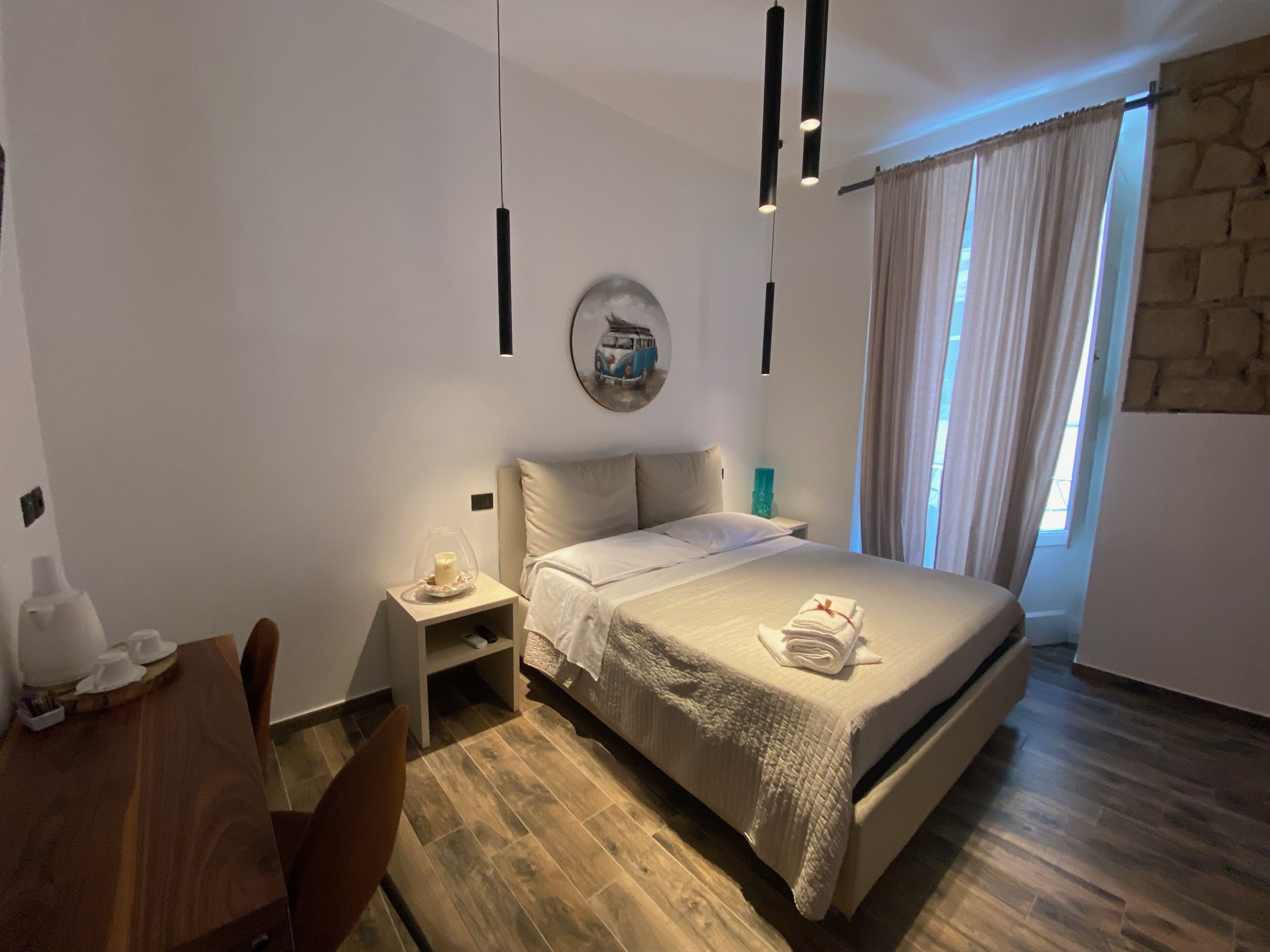 A hotel room with a bed, bedside table, and a small seating area with a chair.