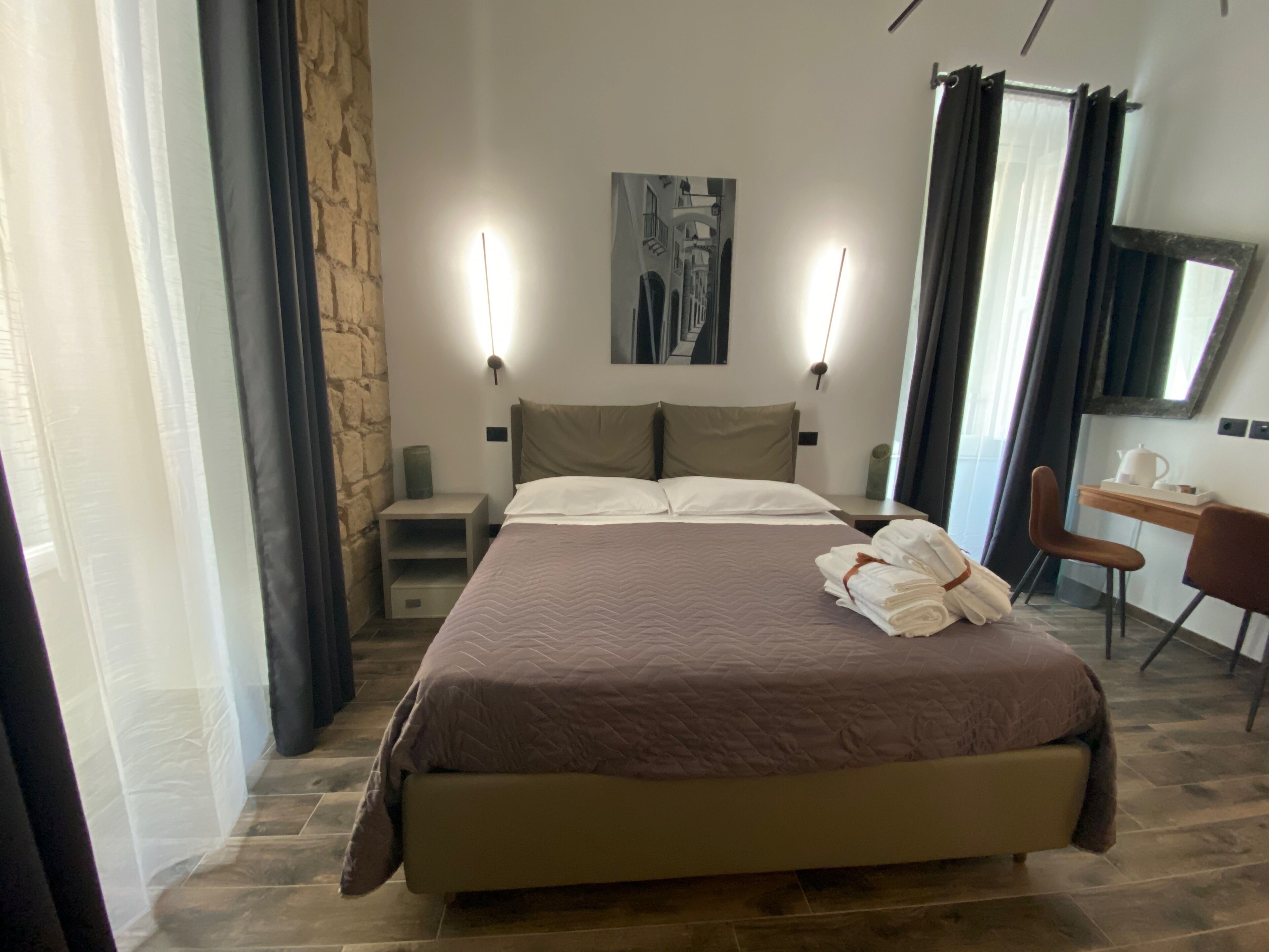 Habitación de hotel con una cama grande, un escritorio con silla, un espejo y un cuadro en la pared.