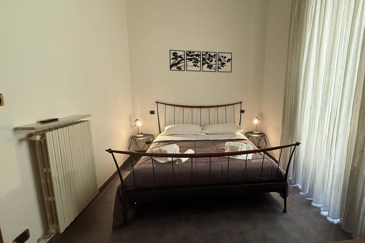 A single bed with a headboard, two bedside tables with lamps, a radiator, and a window with curtains.