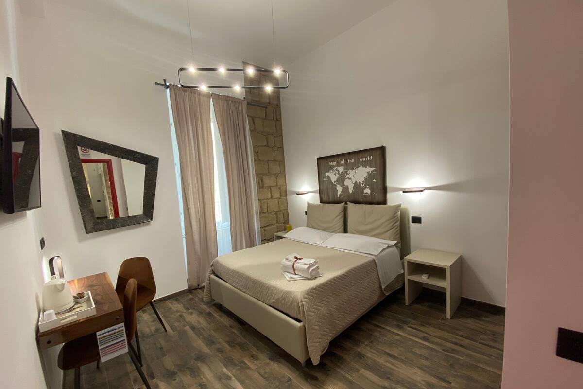 A hotel room with a bed, a desk, a chair, a map on the wall, and a stone accent wall.