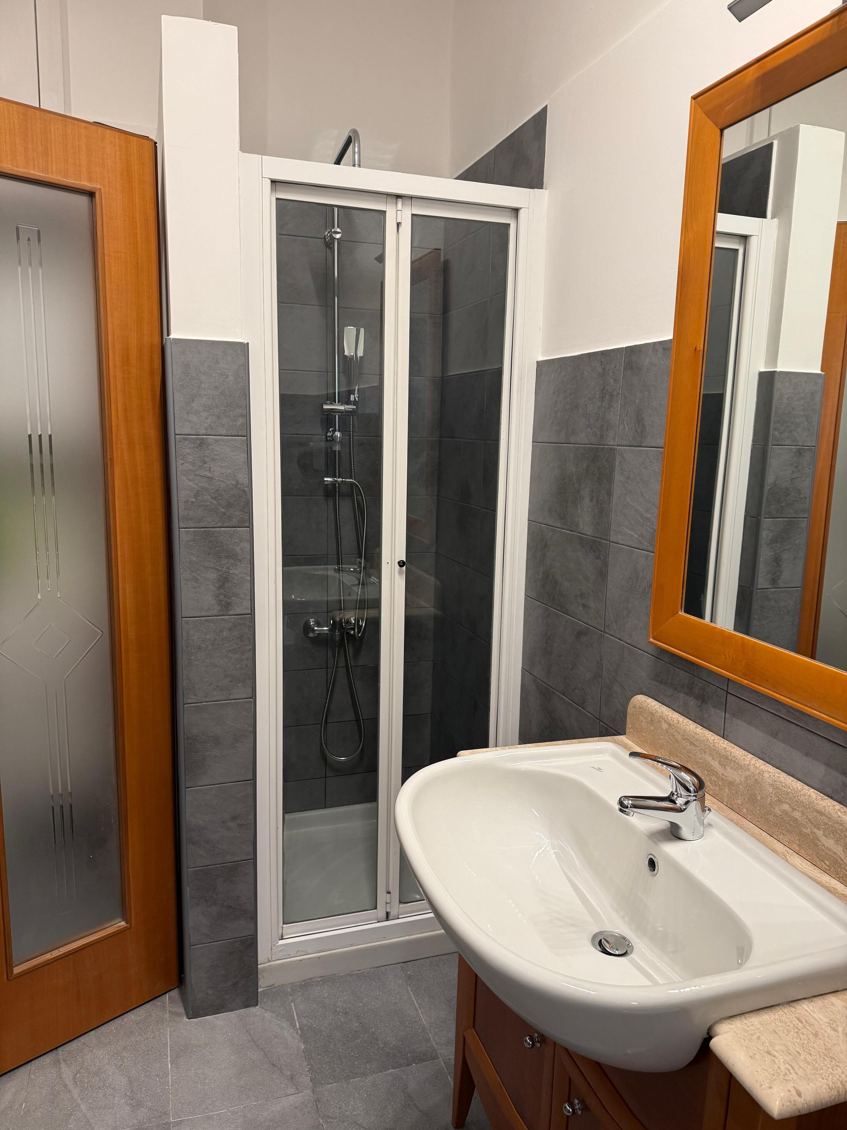A bathroom with a glass-enclosed shower, a white sink, and a wooden vanity.