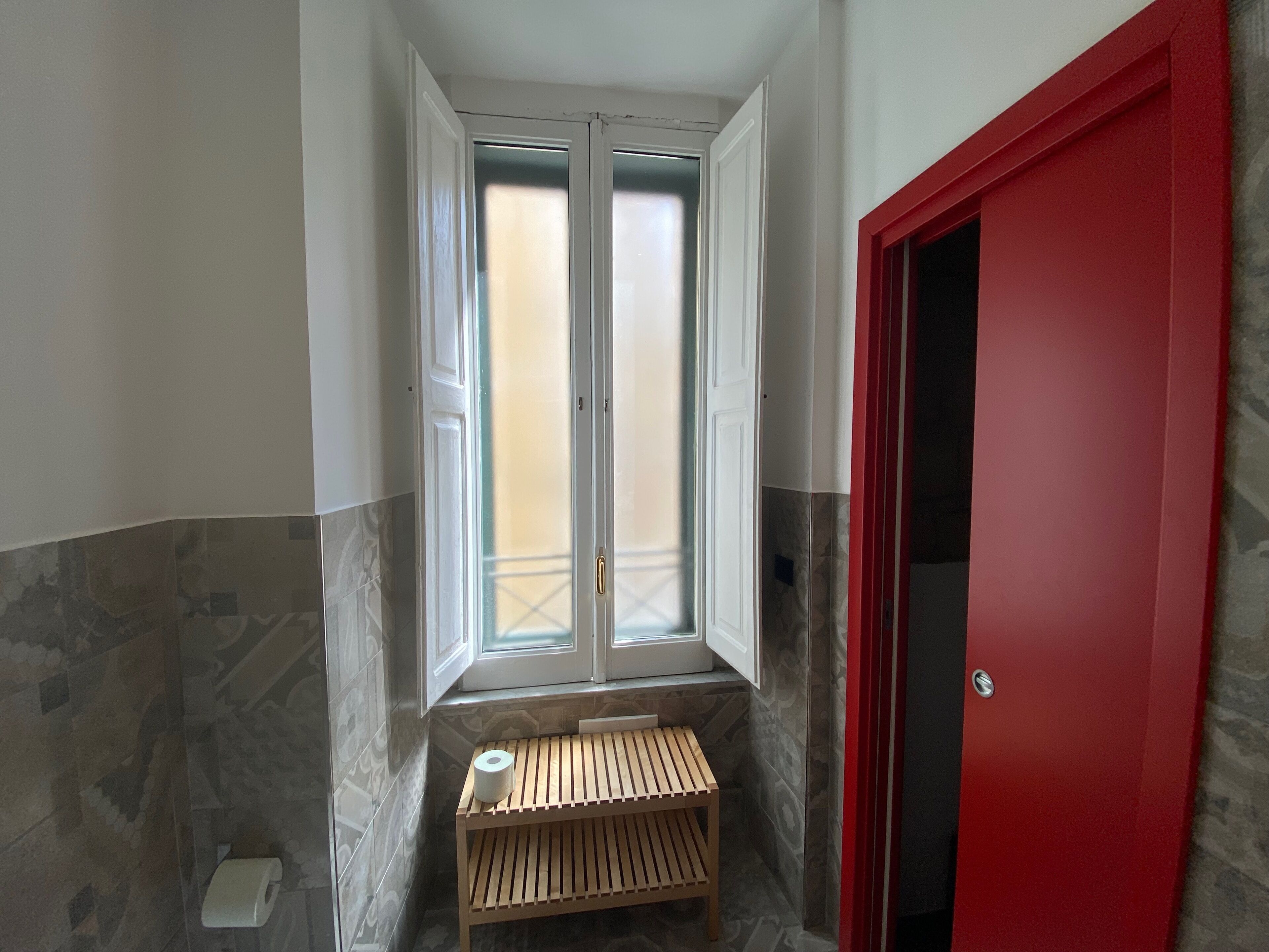 A bathroom with a window, a red door, and a wooden bench.