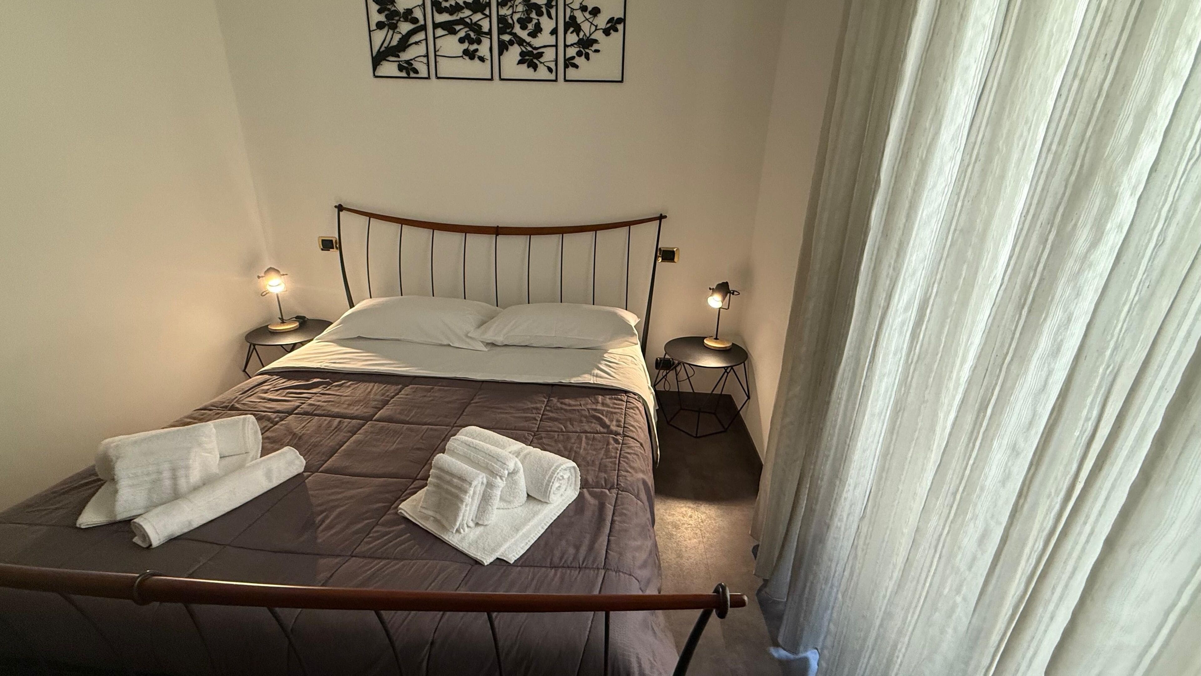 A neatly made bed with a brown quilt, two bedside tables with lamps, and a wall-mounted artwork above the bed.