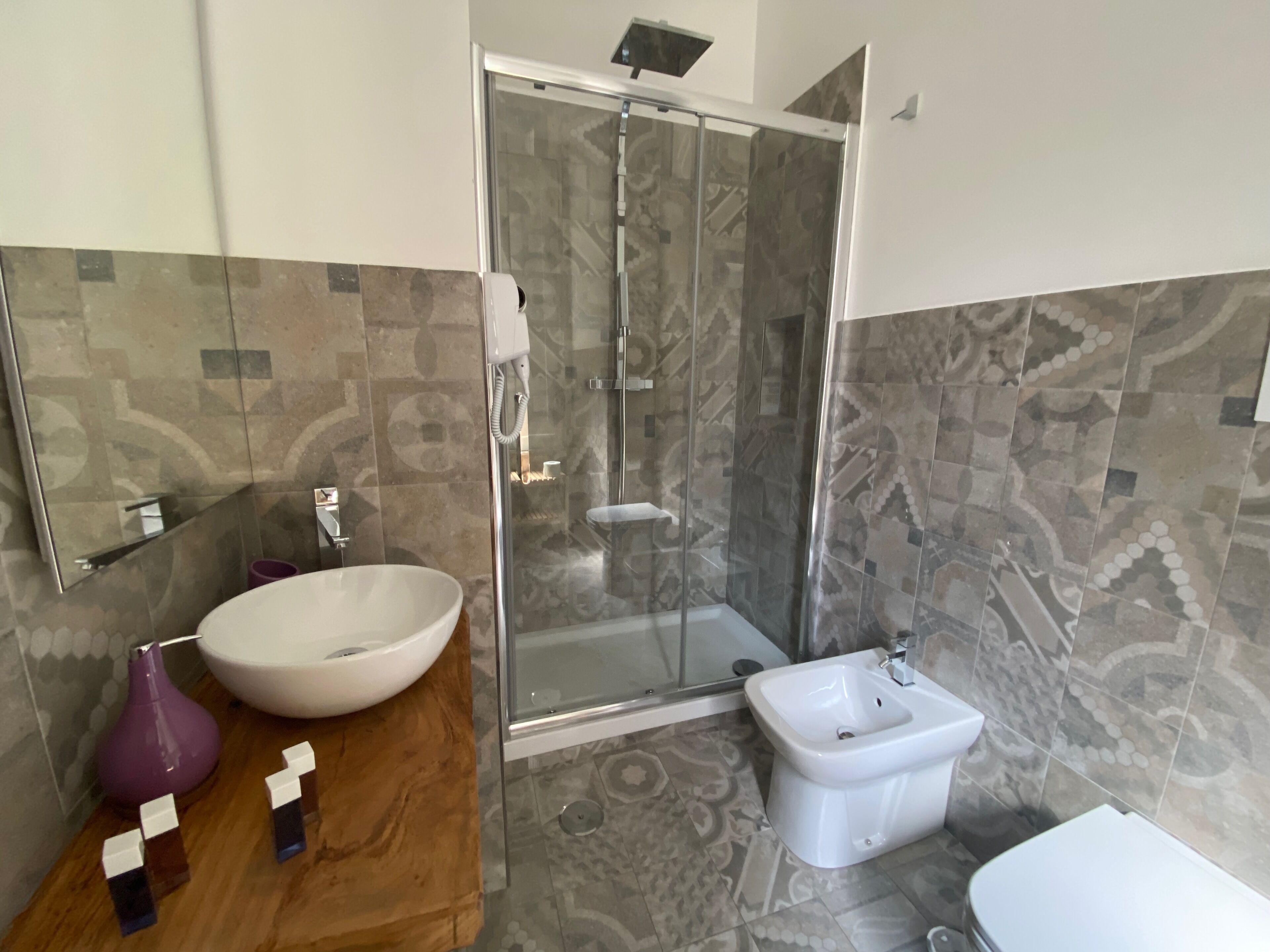A modern bathroom with a glass-enclosed shower, a large white basin, a bidet, and patterned tiles.