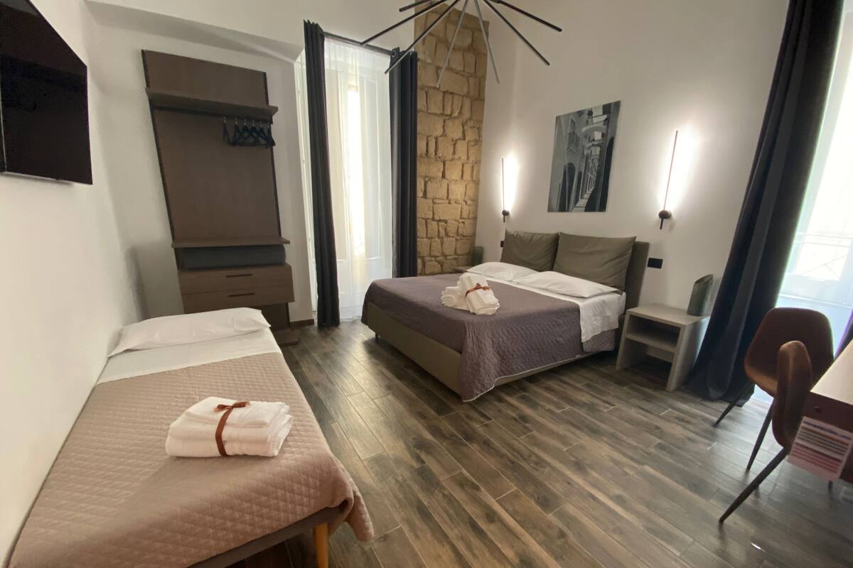 A hotel room with two beds, a stone accent wall, a painting, and a desk with a chair.