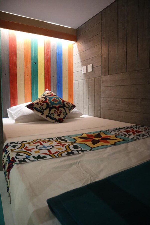 A bed with a colorful striped headboard, a patterned pillow, and a multicolored bedspread. - Write Hostel (Penida Island)