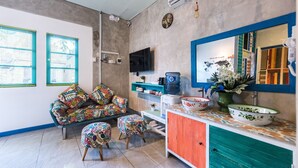 A living room with a sofa, ottomans, a coffee table, a TV, and a water dispenser. - Write Hostel (Penida Island)