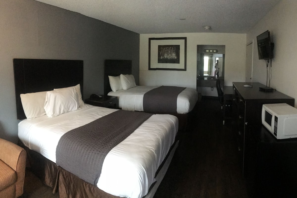 A hotel room with two beds, a desk, a chair, a television, and a microwave.