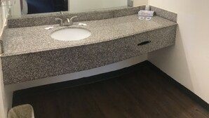 A bathroom with a granite countertop, a sink, a mirror, a towel rack, and a hand dryer. - Texas Inn (Rosenberg)