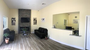 A spacious living room with a stone fireplace, a black leather sofa, a coffee table, and a large mirror. - Texas Inn (Rosenberg)