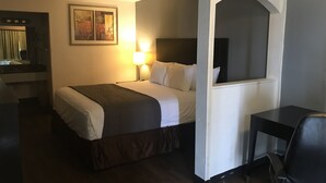 A hotel room with a bed, bedside table, lamp, and a desk with a chair. - Texas Inn (Rosenberg)