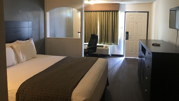 A hotel room with a large bed, a desk, a chair, a television, and a wardrobe. - Texas Inn (Rosenberg)