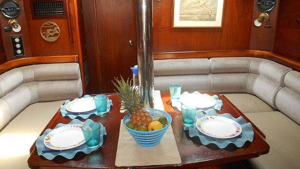 Een eetgedeelte met een houten tafel gedekt voor twee personen, met een ananas en een schaal fruit.