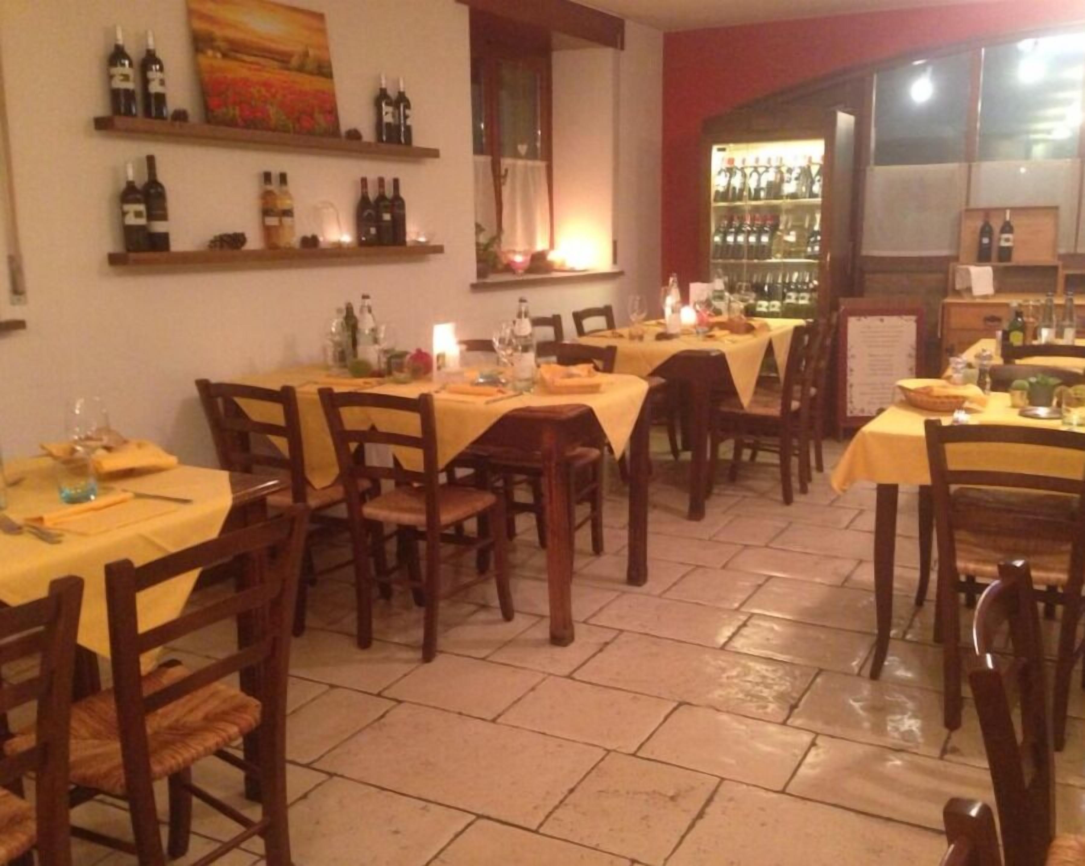 Ein Restaurant mit mehreren Tischen, gedeckt mit gelben Tischdecken, Holzstühlen und Regalen mit Weinflaschen.