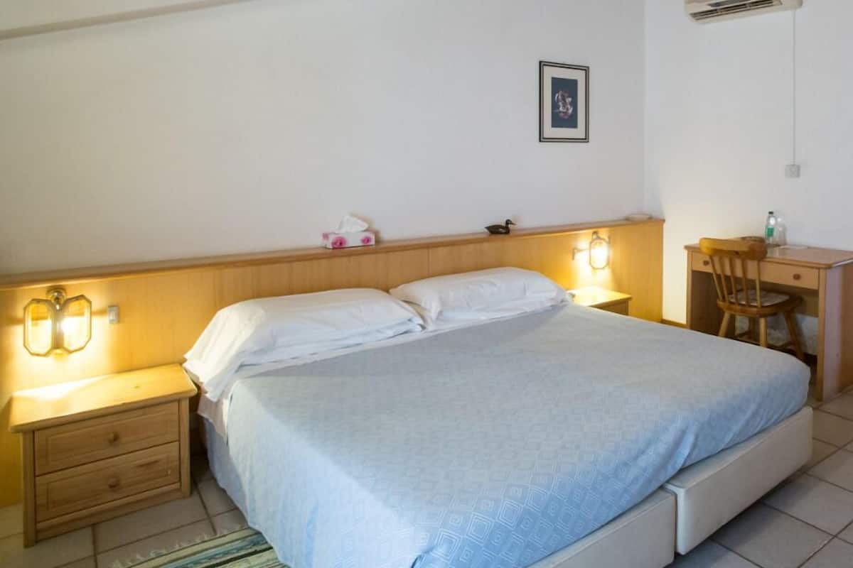 A bedroom with a bed, bedside tables, a desk, and an air conditioning unit.