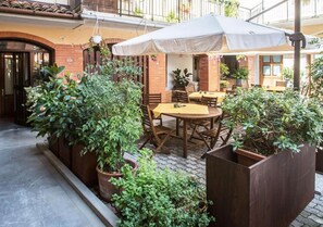Un área de estar al aire libre con mesas y sillas, rodeada de plantas en macetas.