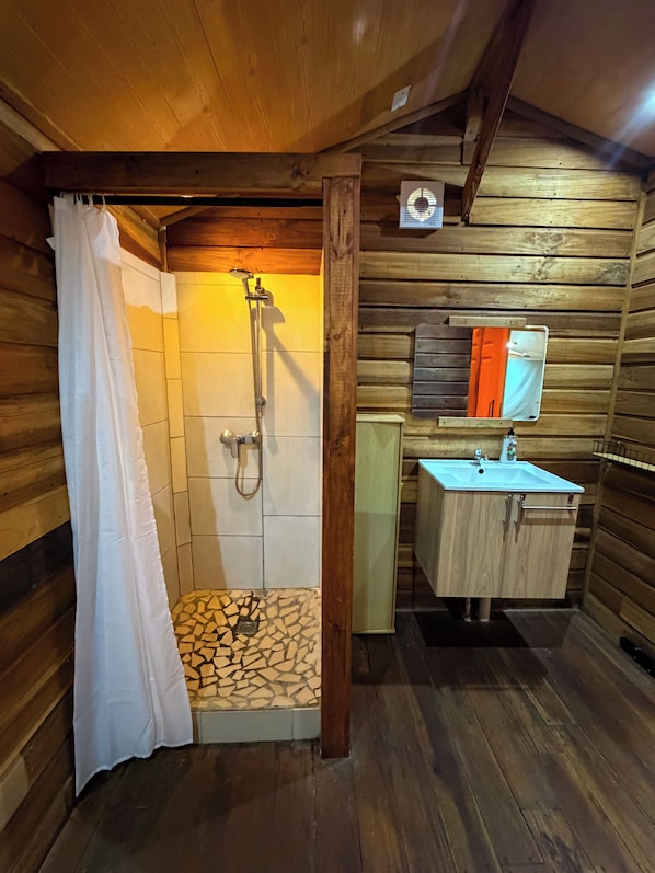Baño de cabaña de madera con ducha, lavamanos y piso de baldosas.