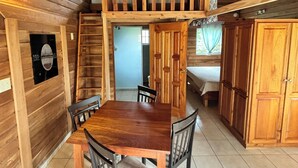 Interior de madera con una mesa de comedor, sillas, un ventilador de techo y una zona de entrepiso.