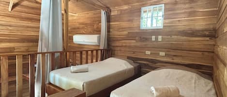 Una cabaña de madera con dos camas, un ventilador de techo, una ventana y un equipo de aire acondicionado.
