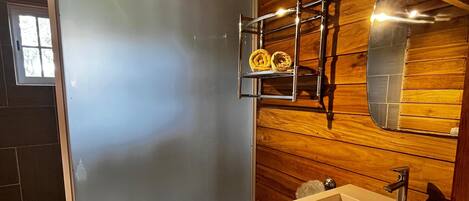 Un baño moderno con mampara de vidrio, lavamanos con espejo y paneles de madera.
