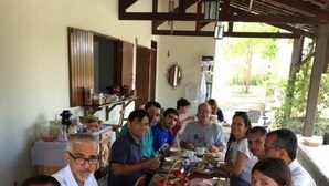 A group of people dining at a long table in a covered outdoor area with a rustic wooden ceiling and walls. - Macambira Café Pousada (Delmiro Gouveia)