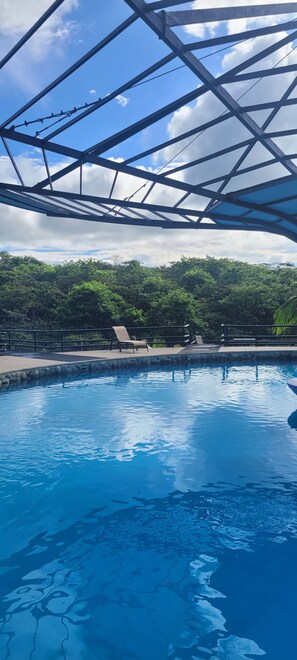 Une piscine à l’eau d’un bleu cristallin, entourée de chaises longues et surmontée d’une structure de toit en métal.