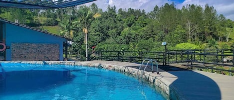 Una piscina con borde de piedra, cubierta de madera y escalera de metal.