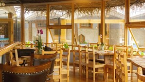 Een restaurant met houten tafels en stoelen, grote ramen en een rieten dak.