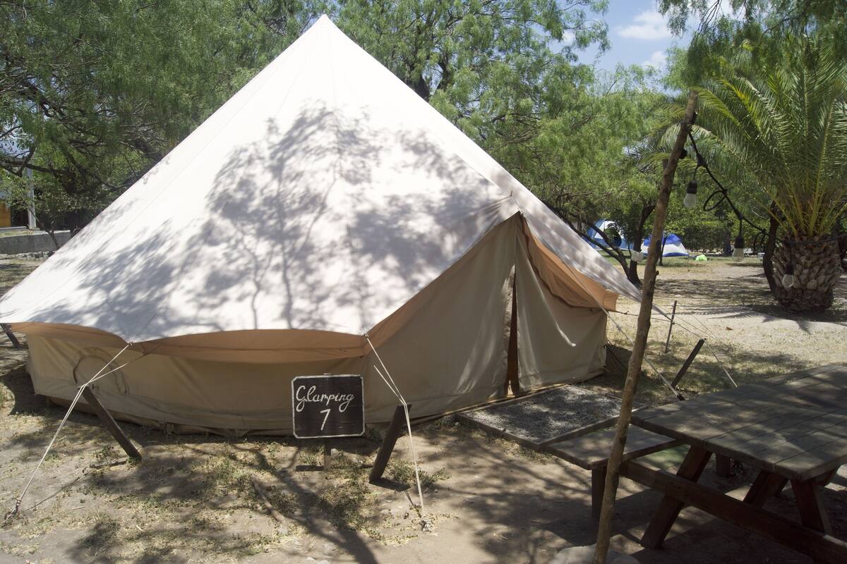 Una gran carpa con un cartel que dice "Clamping 7" en un camping con árboles y una mesa de picnic.
