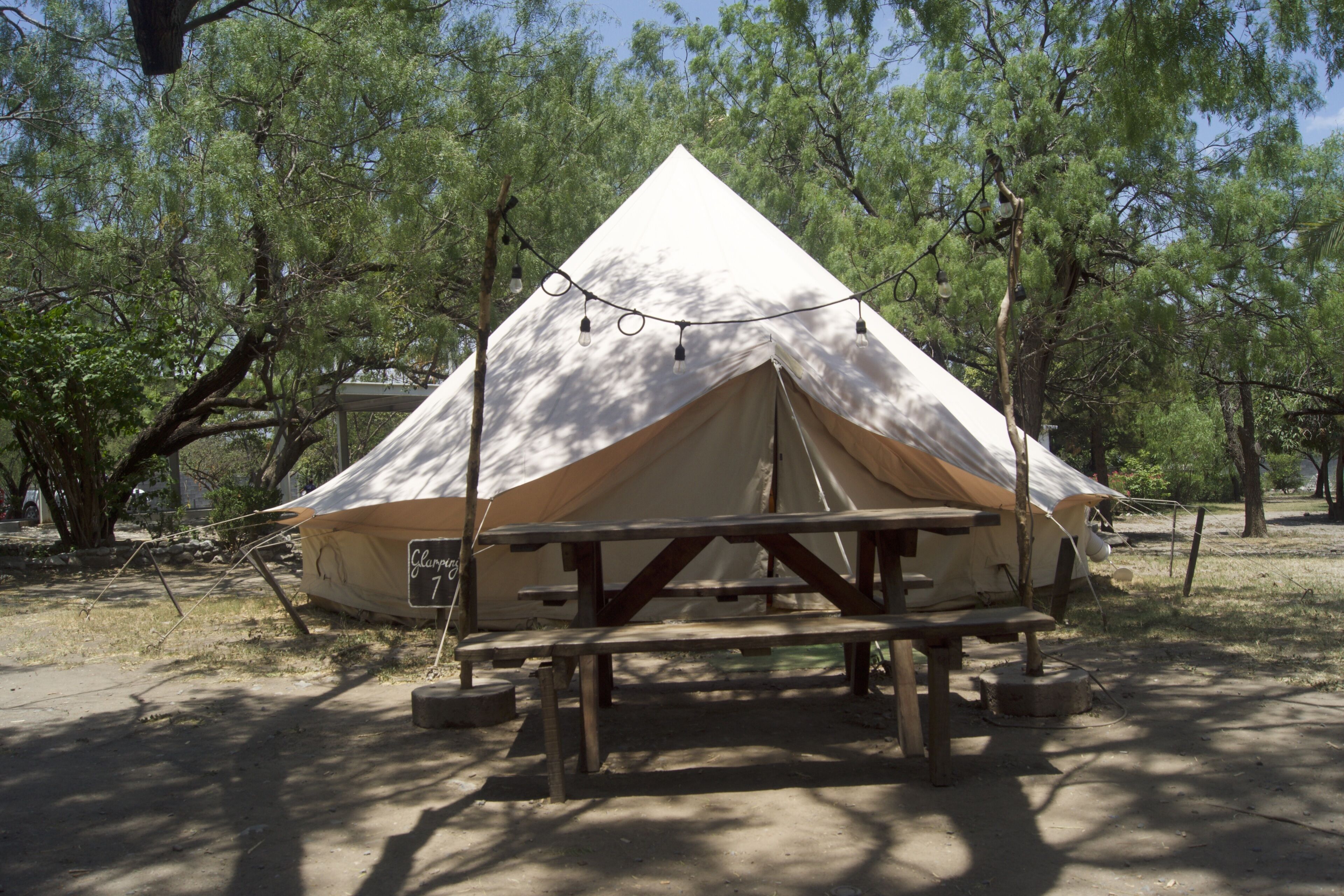 Una gran tenda en forma de piràmide amb una taula de pícnic al davant, envoltada d'arbres.