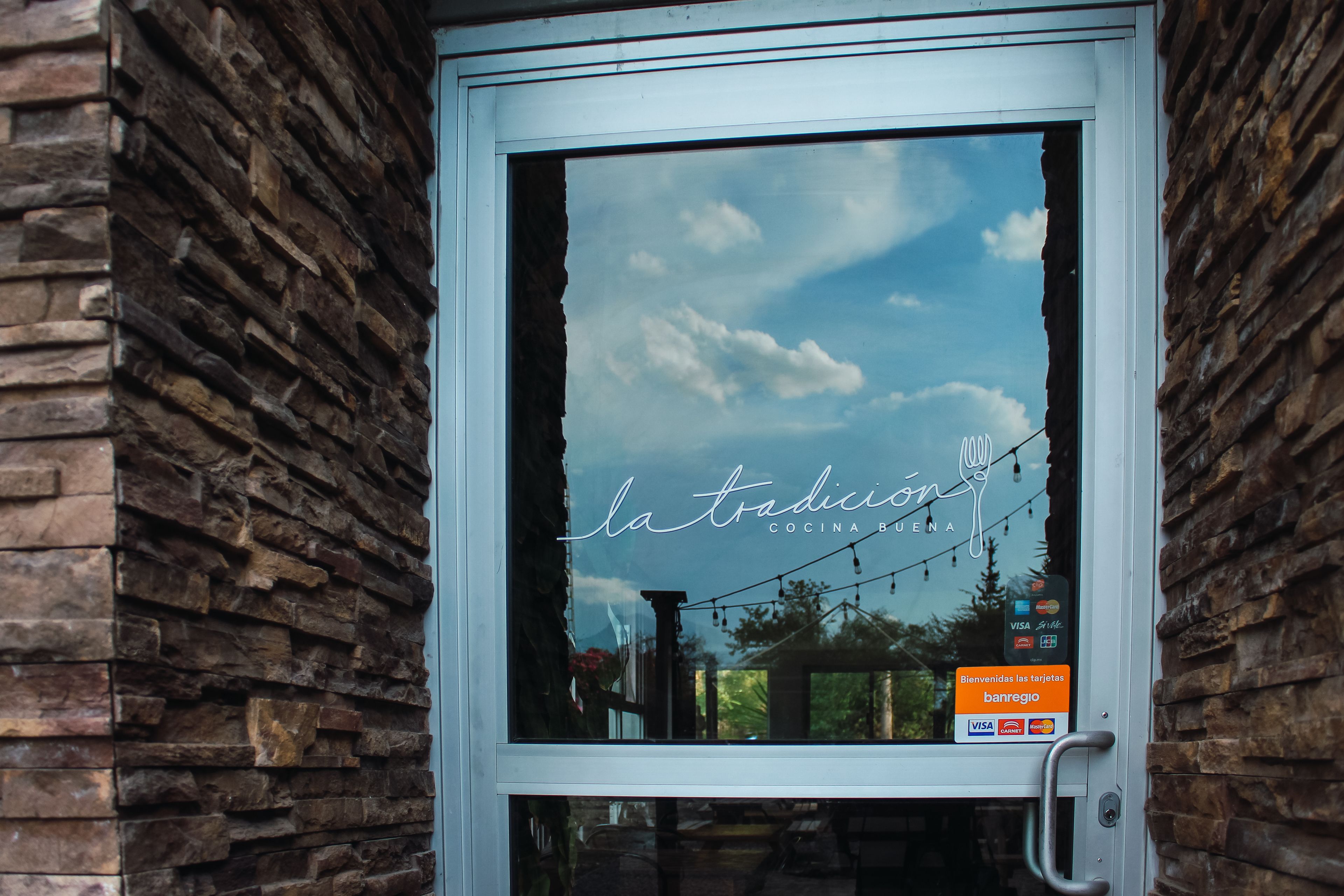 A window with a stone wall, a sign reading "la tradición," and a Visa acceptance sign.