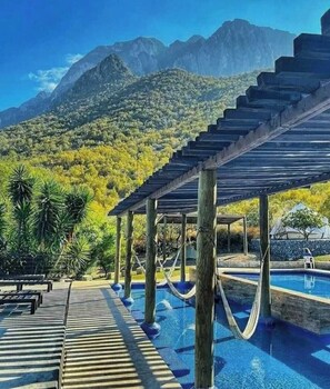 Zona de piscina amb una pèrgola de fusta, una piscina i un paisatge de muntanyes al fons.