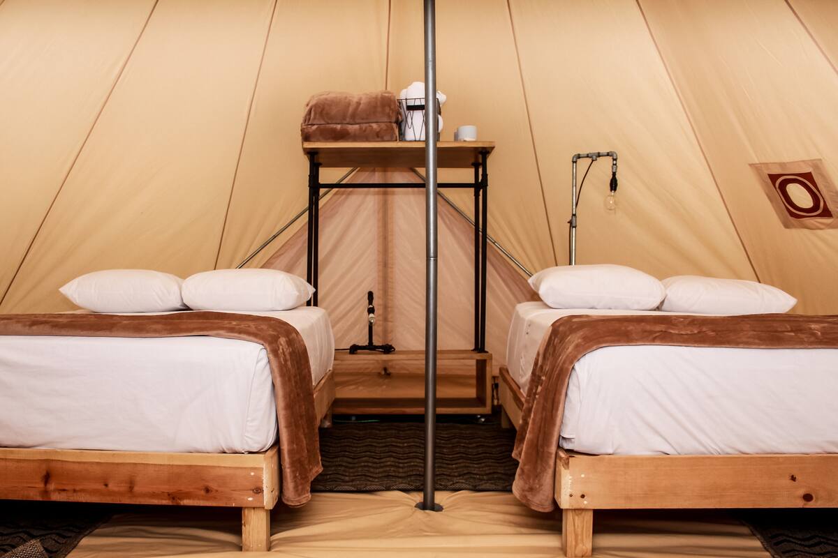 Una carpa con dos camas, una mesa con una lámpara y un estante con objetos.