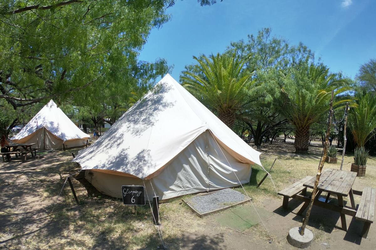Un camping con dos tiendas de campaña blancas, mesas de picnic y un cartel que indica la tienda número 6.