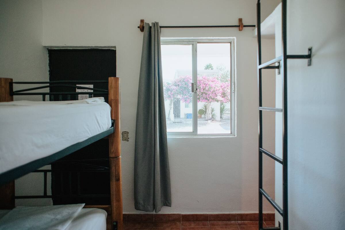 Un dormitorio con literas, una ventana con cortina y una escalera.
