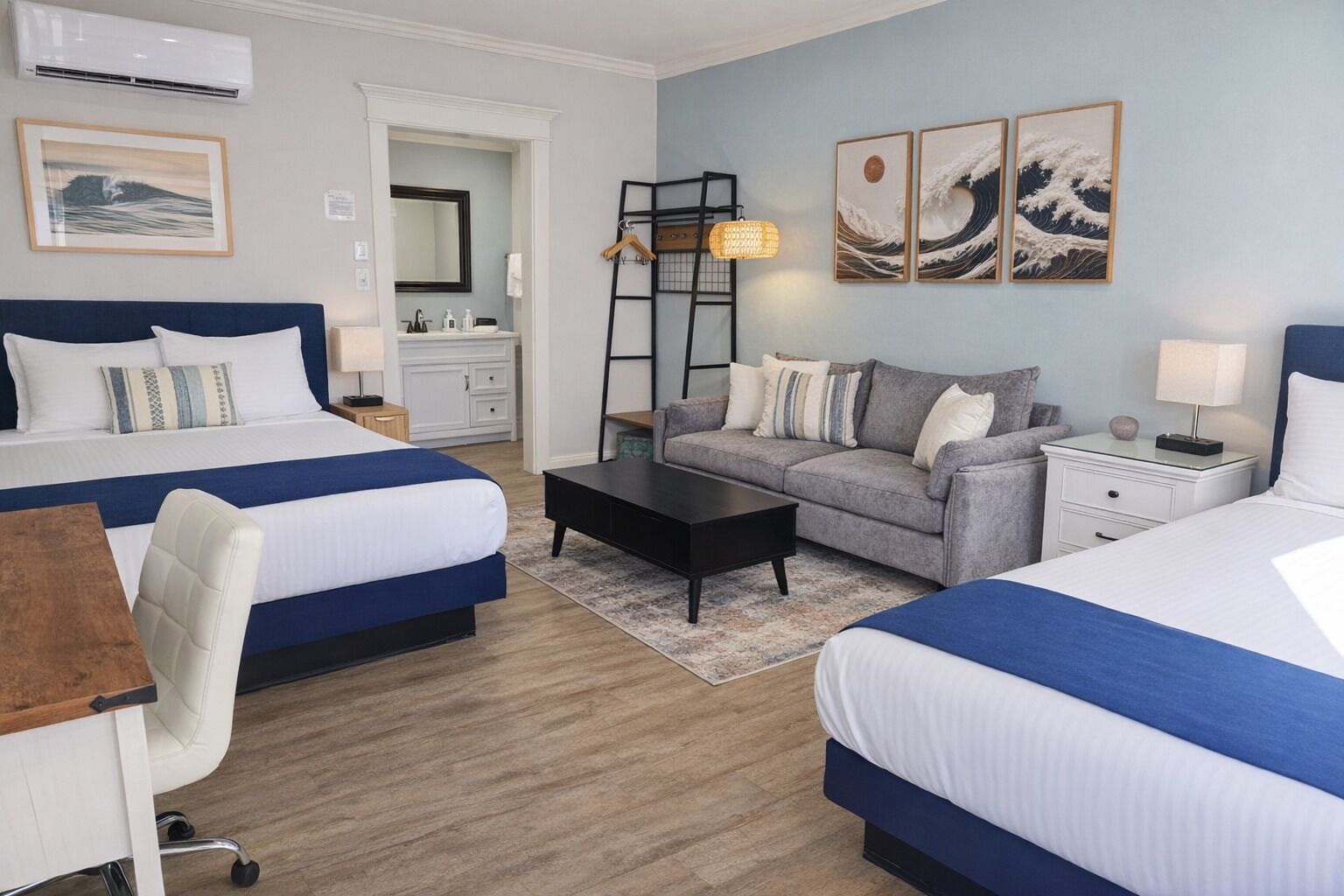 A hotel room with two beds, a sofa, a desk, and a chair. There is a mirror, a dresser, and artwork on the walls.