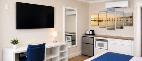 A hotel room with a bed, a desk with a chair, a flat-screen TV, a microwave, a refrigerator, and a large mirror.