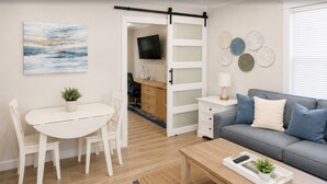 A modern living room with a dining area, a grey sofa, a TV, and a sliding door leading to a kitchen. - Coronado Inn (Coronado)