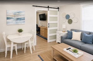A modern living room with a dining area, a grey sofa, a TV, and a sliding door leading to a kitchen.