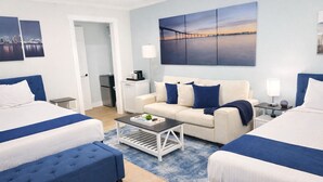 A hotel room with two beds, a sofa, a coffee table, and a large wall painting. - Coronado Inn (Coronado)