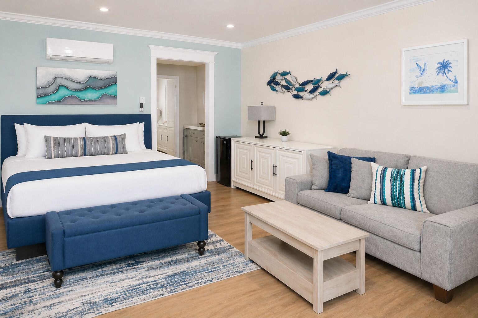A bedroom with a bed, a grey sofa, a coffee table, and artwork on the walls.