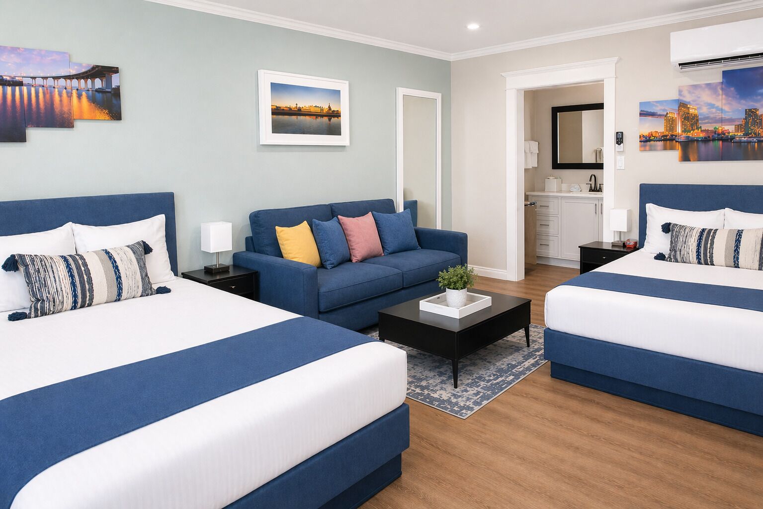 A hotel room with two beds, a sofa, a coffee table, and artwork on the walls.